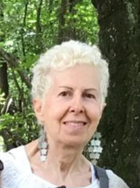 a smiling face of a mid-aged woman with trees behind